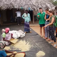 Students from Switzerland watch Indian women in the traditional processing of grain.