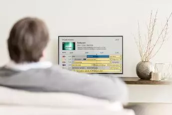 Bild: Person sitzt vor Fernseher, welcher Bedienoberfläche von Swisscpm TV zeigt