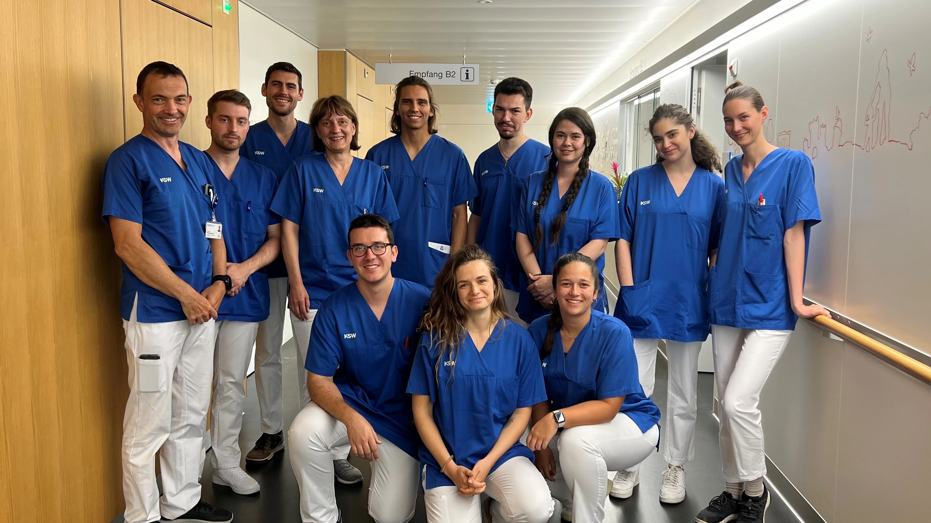 Gruppenbild von Personen in blauen Hemden und weisser Hose in einem Flur eines Krankenhauses.