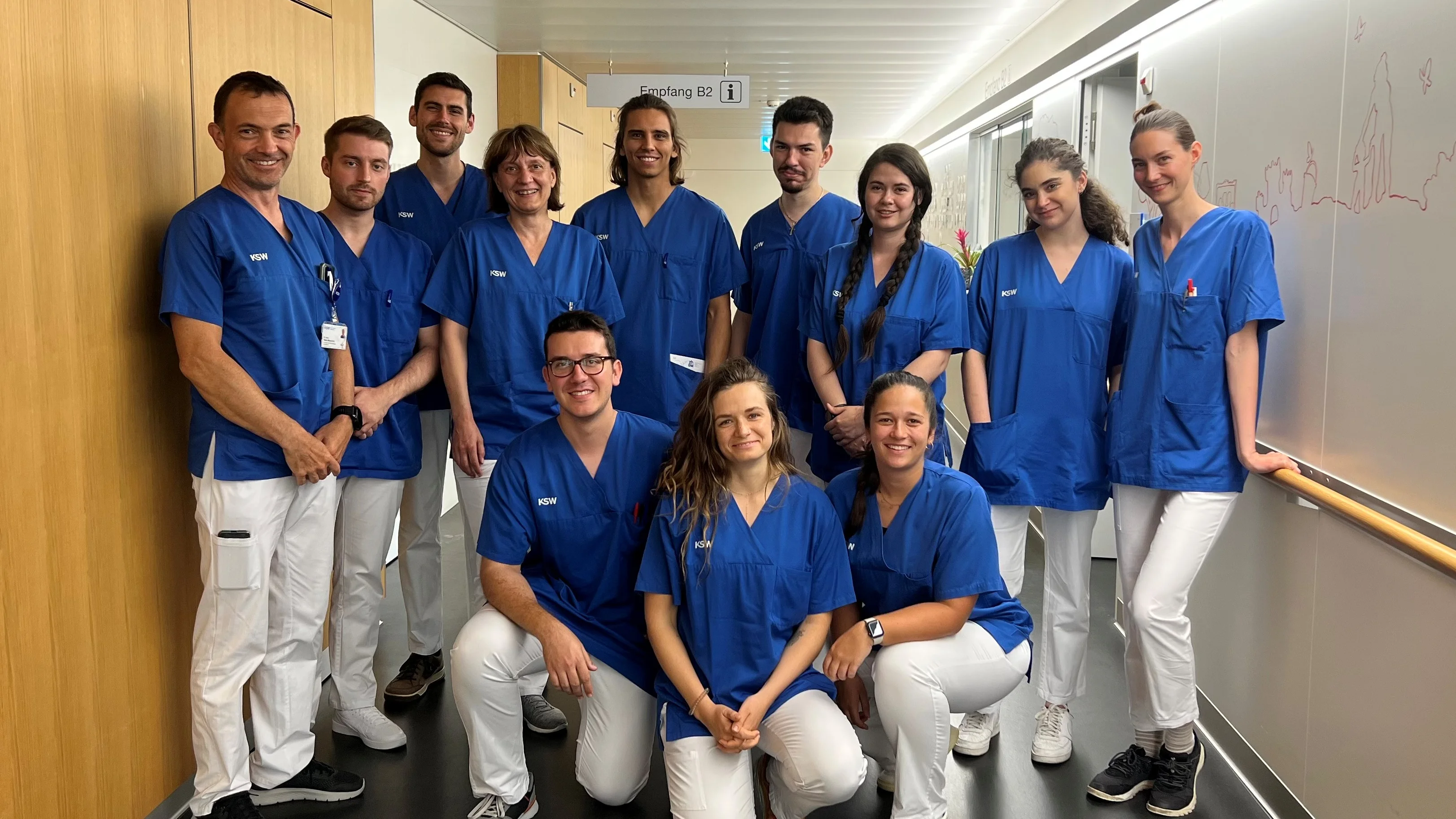 Gruppenbild von Personen in blauen Hemden und weisser Hose in einem Flur eines Krankenhauses.