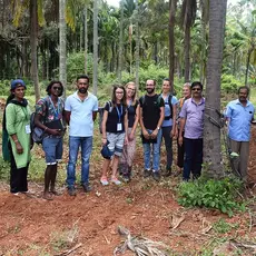 Summer School participants stand in a cocoa plantation and smile at the camera.