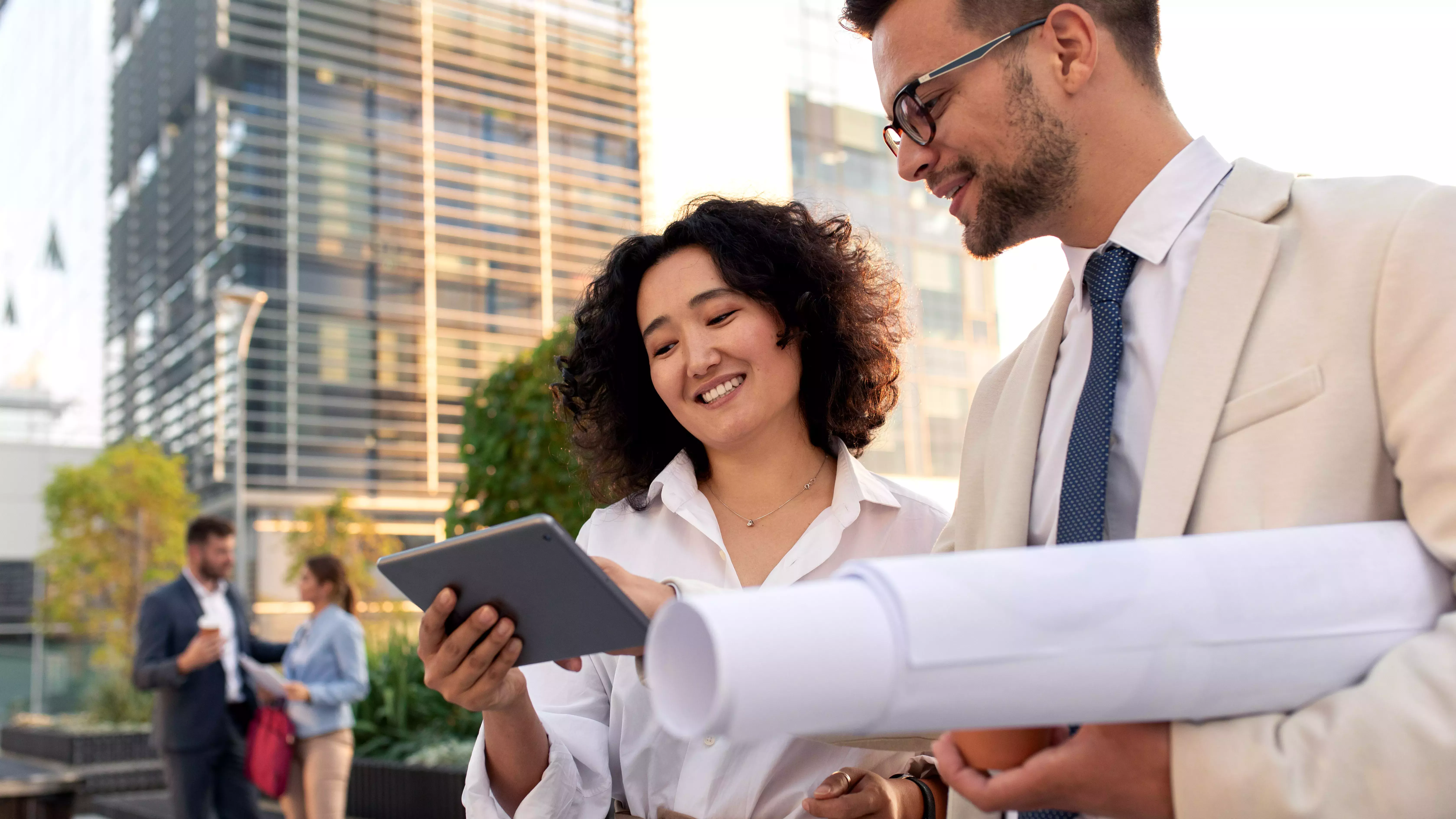 Two coworkers standing outside in front of office buildings discuss about business plan and looking at tablet.