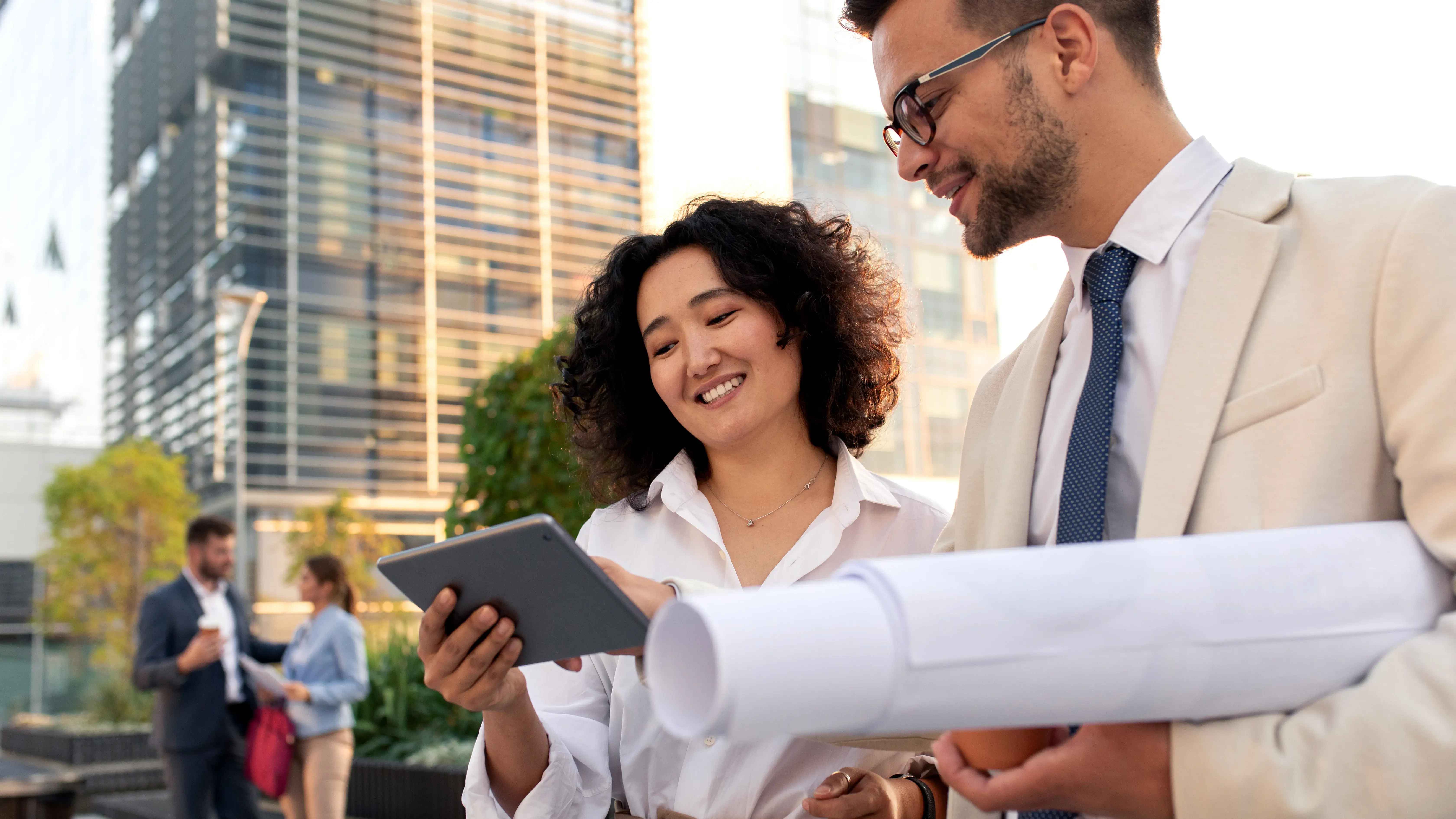 Two coworkers standing outside in front of office buildings discuss about business plan and looking at tablet.