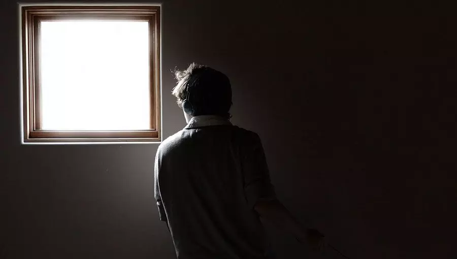 Ein Junge steht im Dunkeln mit dem Rücken zur Kamera und schaut aus einem hell erleuchteten Fenster heraus.