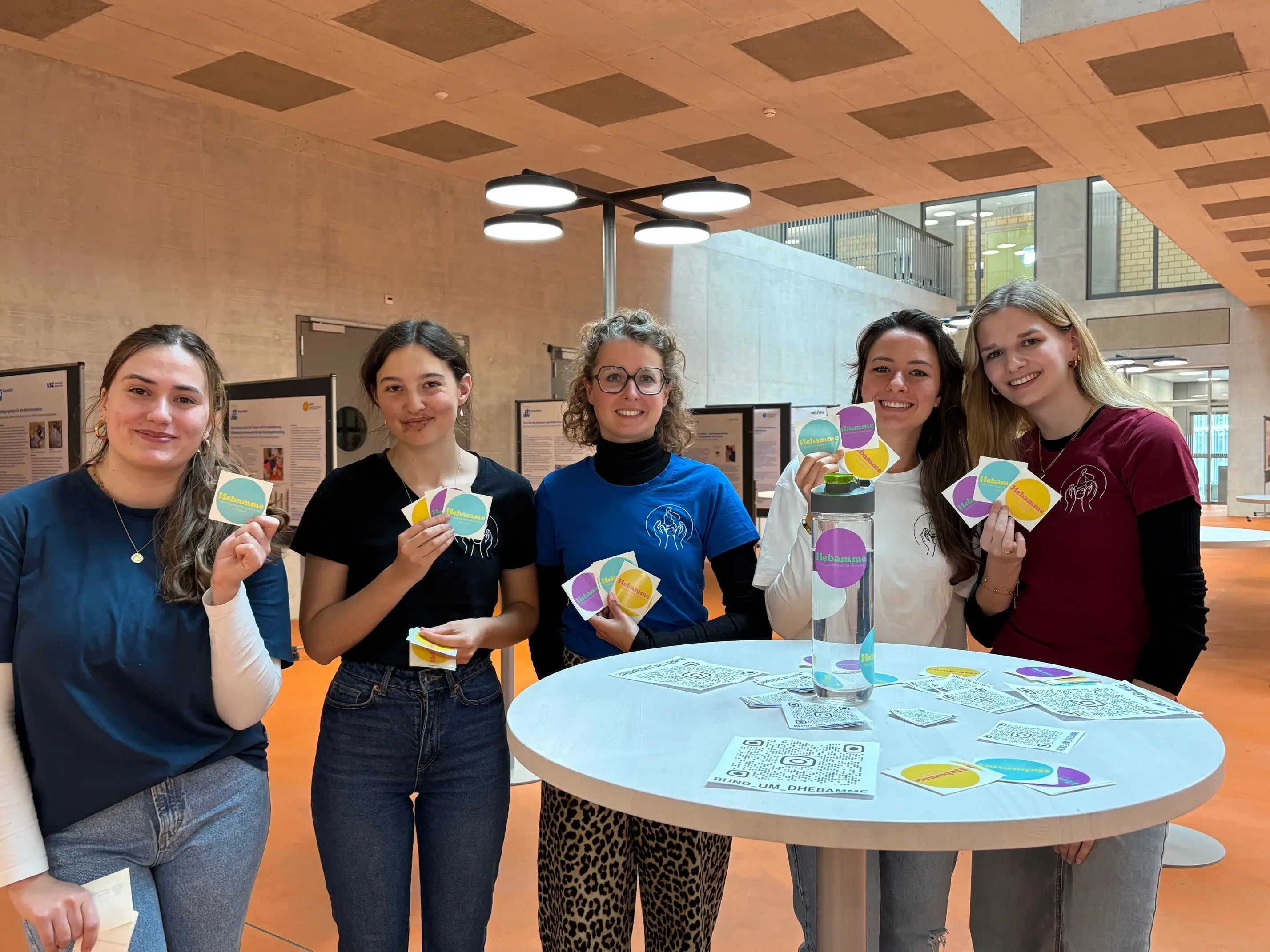 Das Projektteam hält die bunten Sticker, die auf die Schwangerenbetreuung durch Hebammen aufmerksam machen.