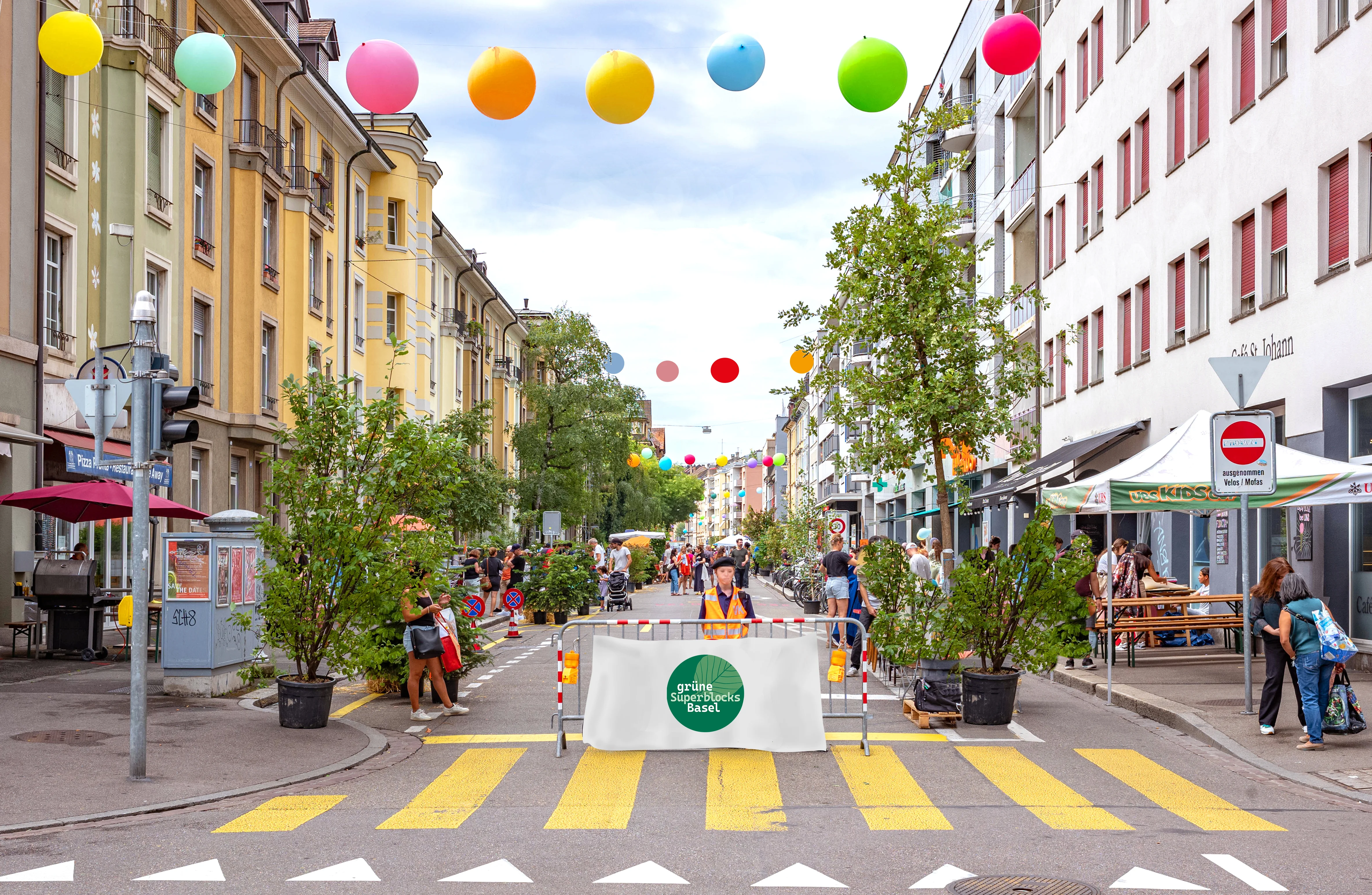 Ein für Autos gesperrter, bepflanzter Strassenabschnitt in Basel, überspannt von einer Girlande bunter Ballons. Ein Werbebanner mit dem Text „Grüne Superblocks Basel“ blockiert die Fahrbahn.