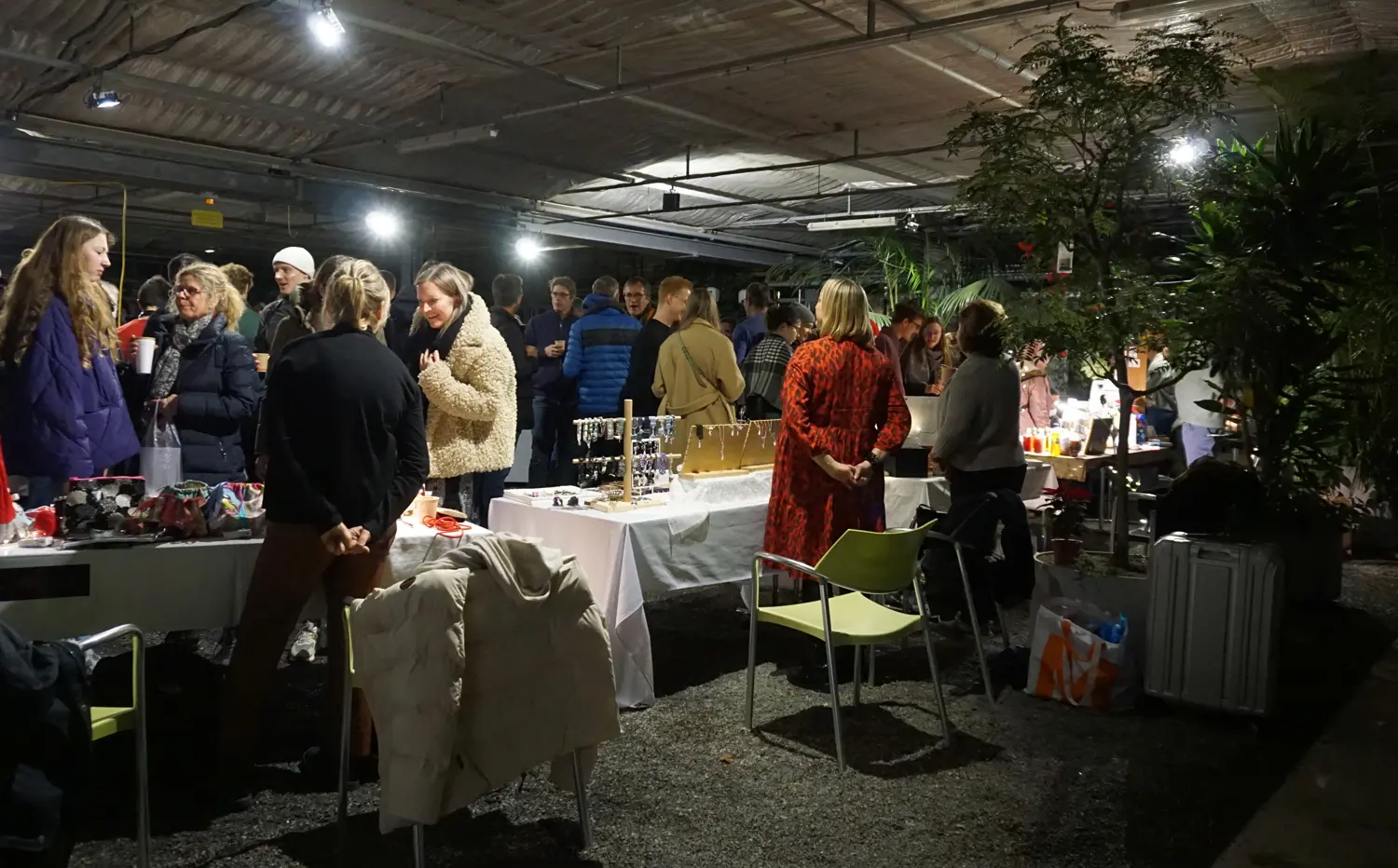 Eine Gruppe Personen, die in einer Halle stehen, im Vordergrund Tische mit angebotenen Waren.