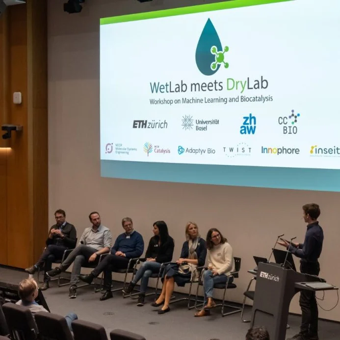 Leute auf der Bühne, Folie "WetLab meets DryLab - Workshop on Machine Learning and Biocatalysis" mit den Logos der teilnehmenden Organisationen
