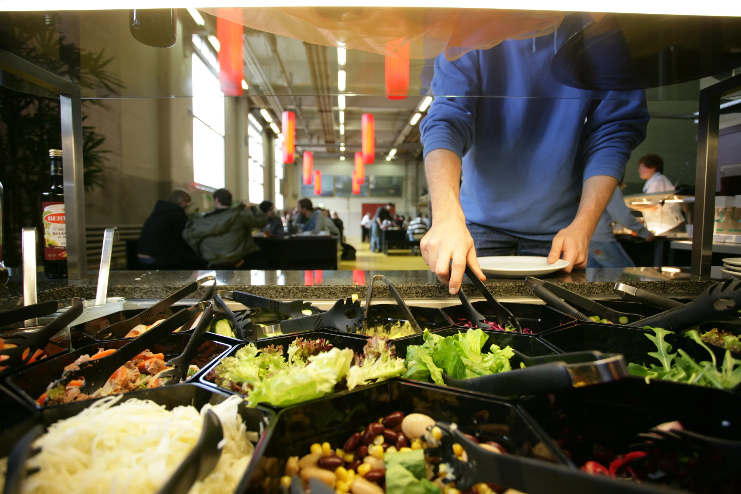 Ein Teil eines Salatbuffets, an welchem sich eine Person bedient.