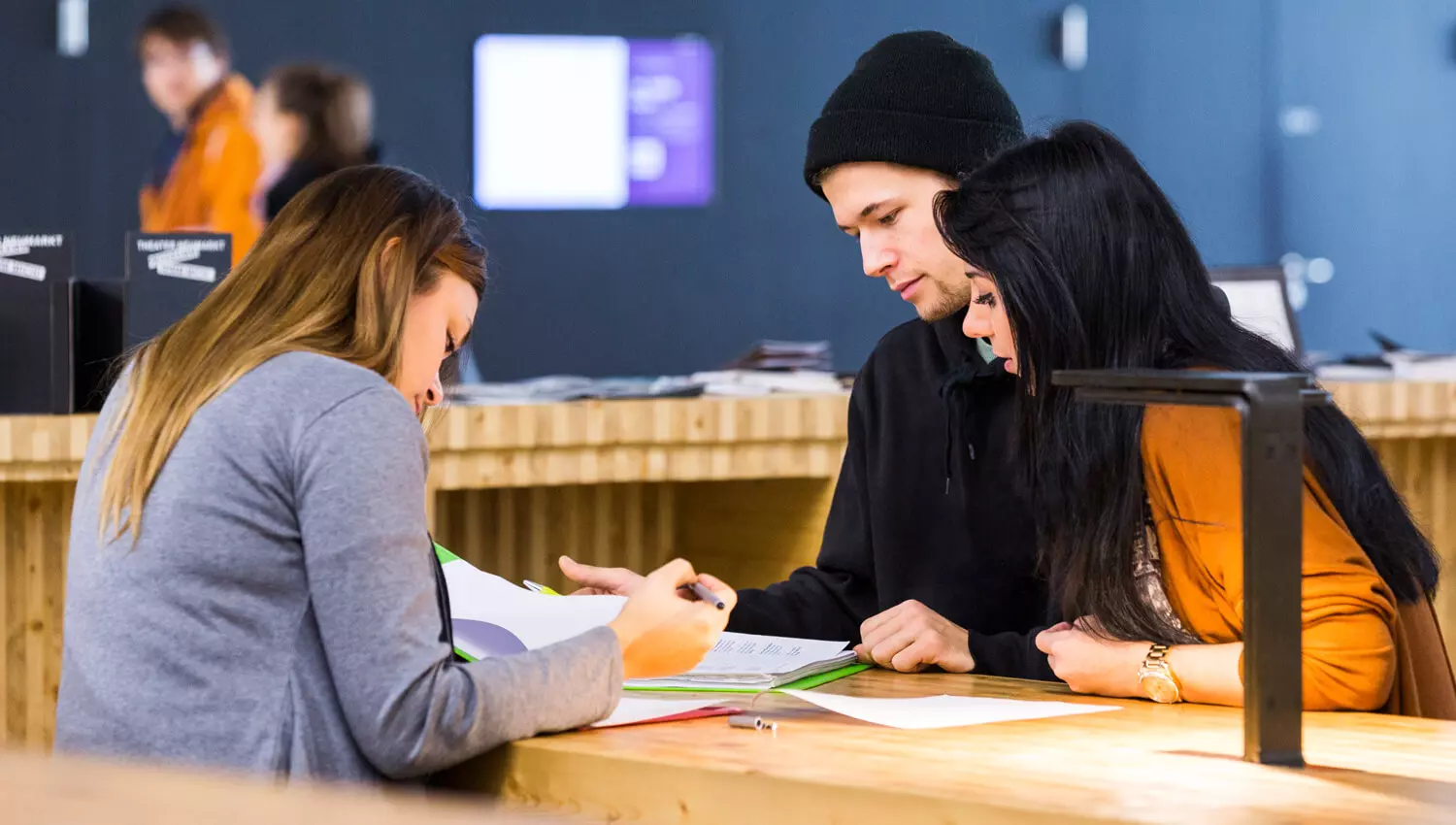 Drei Studierende sitzen einander gegenüber an einem Tisch und schauen in ihre Unterlagen.