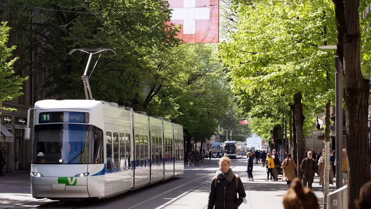 Eine Strassenbahn in Zürich. Im Hintergrund sieht man eine Allee aus Bäumen und Passanten. 