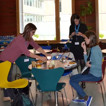 Cafeteria. Eine Gruppe von Konferenzteilnehmenden sitzt um einen Tisch und isst zu Mittag.