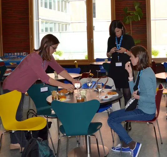 Cafeteria. Eine Gruppe von Konferenzteilnehmenden sitzt um einen Tisch und isst zu Mittag.