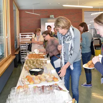 Cafeteria. Einige Konferenzteilnehmende bedienen sich am Mittagsbuffet.