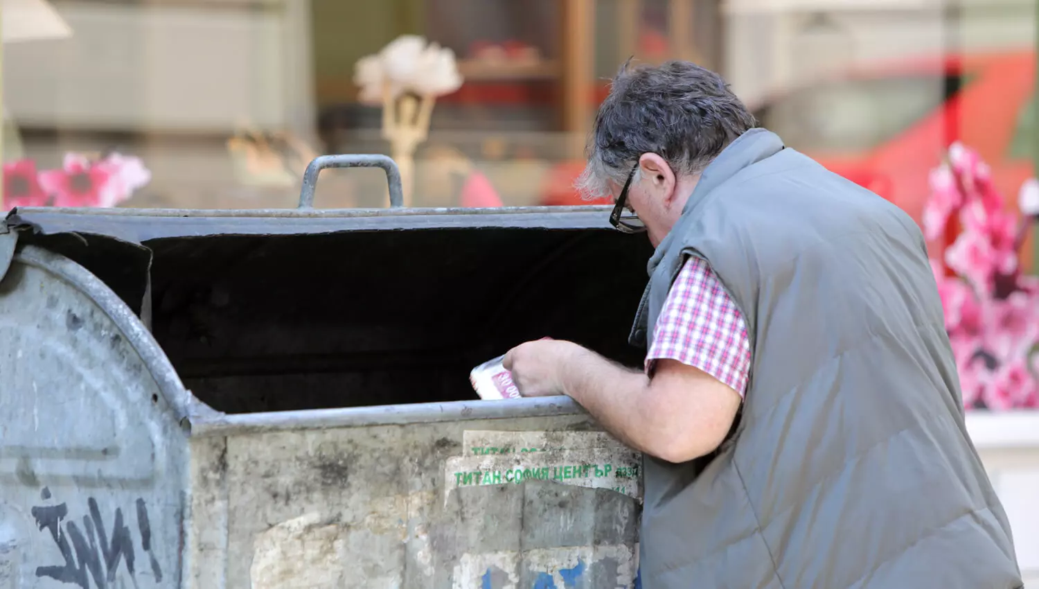 Ein älterer Mann steht vor einer Mülltonne und greift hinein.