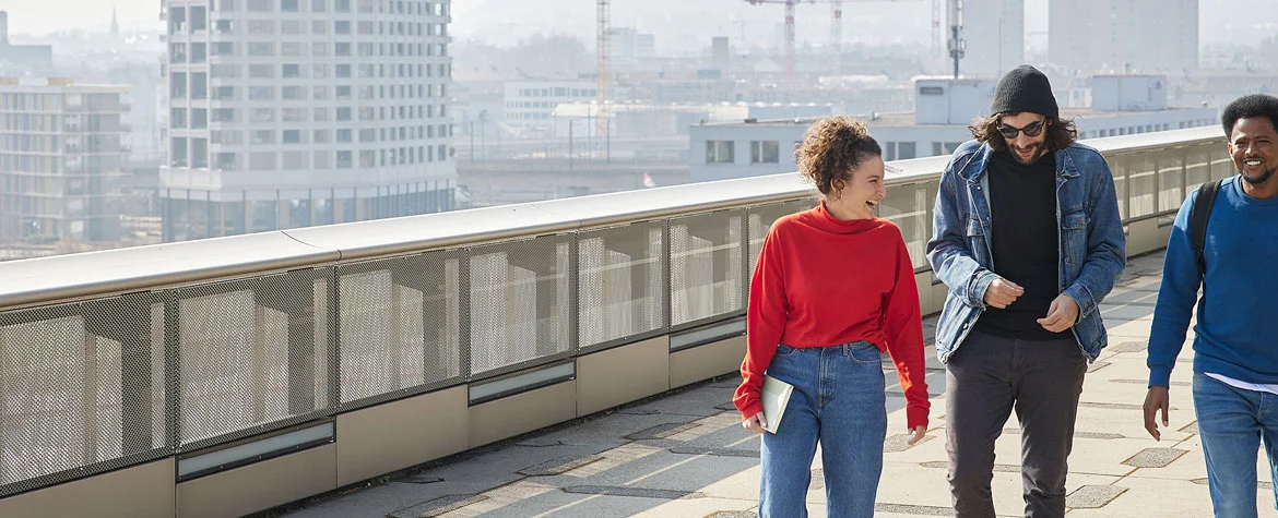 Eine Frau im roten Pulli und zwei junge Männer laufen über die Dachterrasse des Toni-Areals.