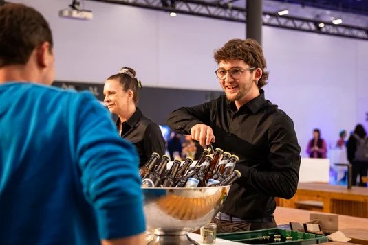 Bild vergrössern: Jemand vom Catering Team schenkt einem Gast ein Getränk aus