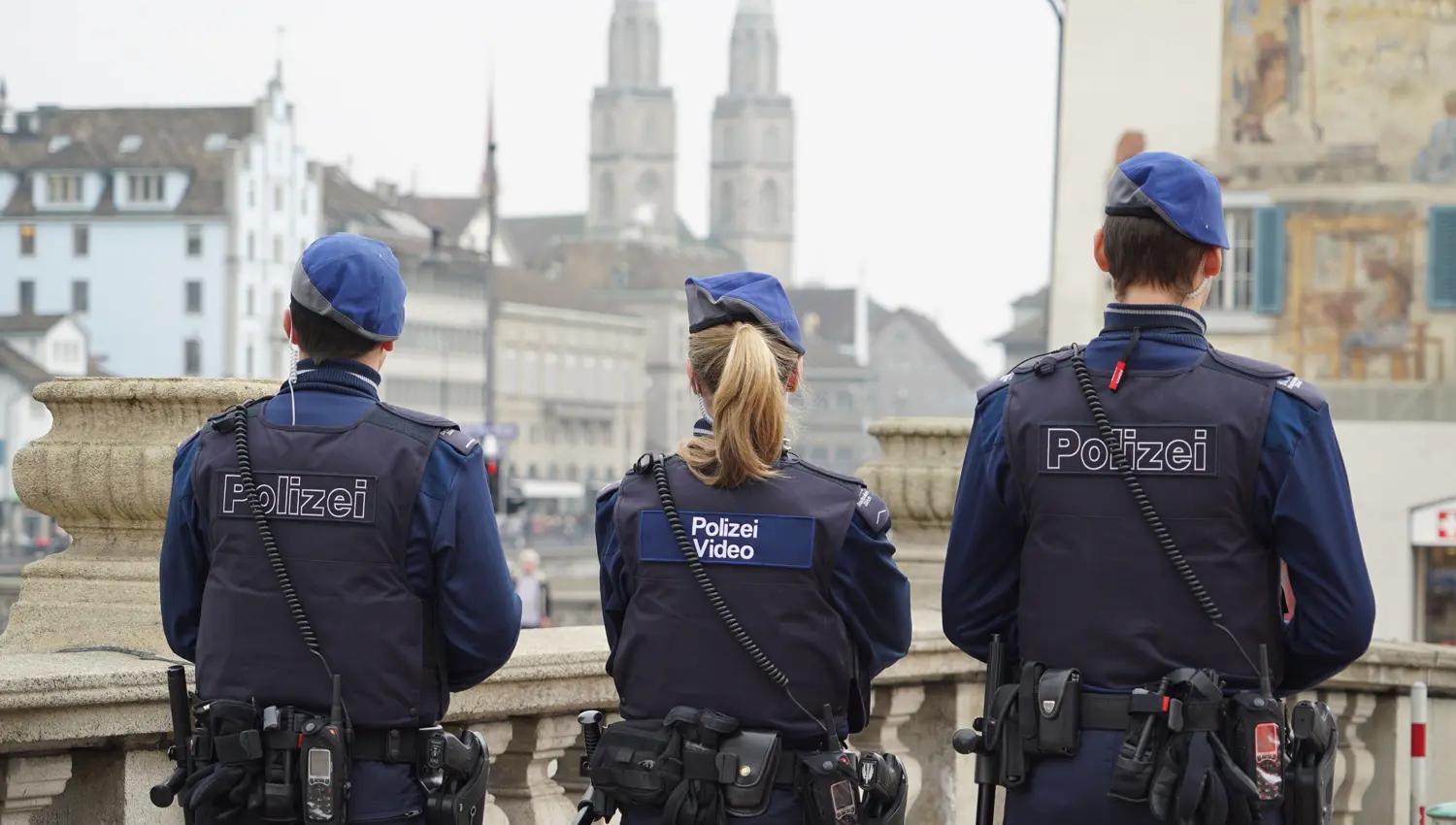 Zwei Polizisten und eine Polizistin stehen mit dem Rücken zur Kamera und schauen auf die Zücher Limmat. Im Hintergrund sieht man das Zürcher Fraumünster.