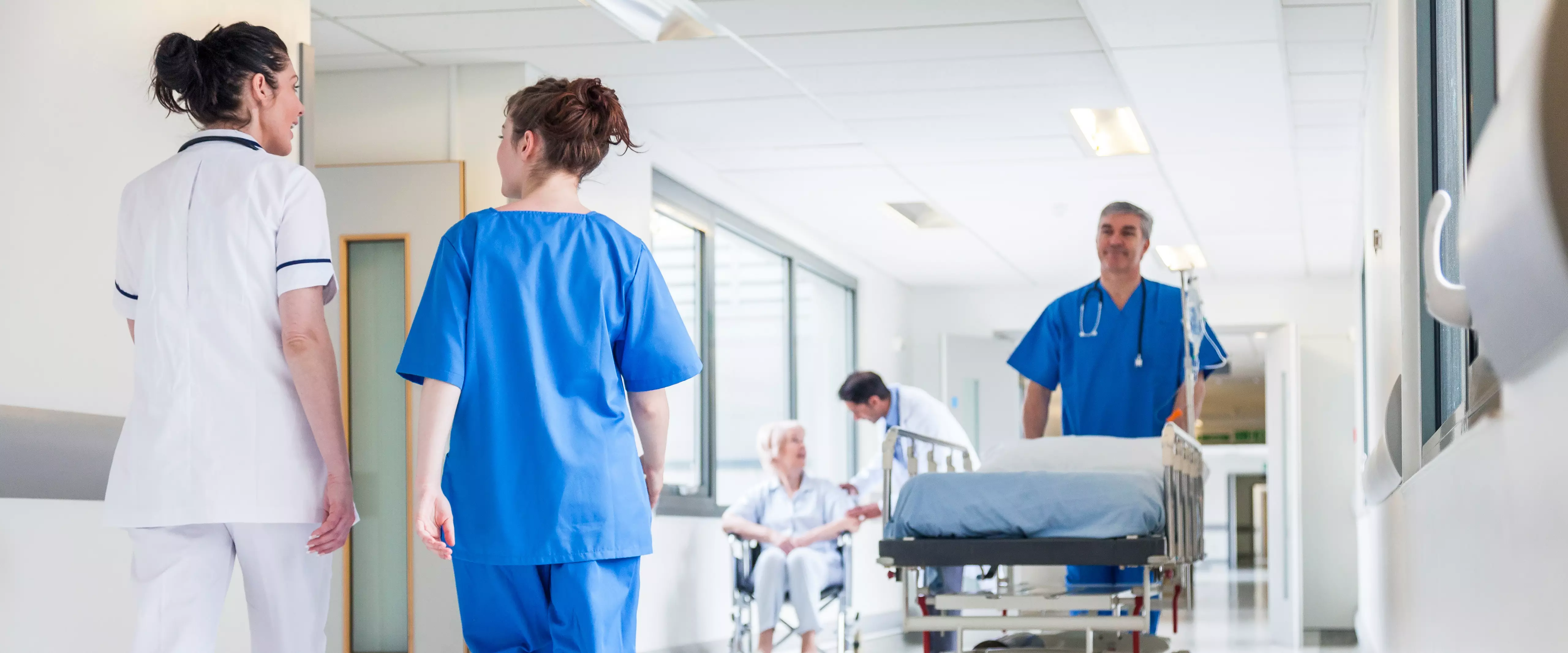 Male nurse pushing stretcher gurney bed in hospital corridor with doctors & senior female patient