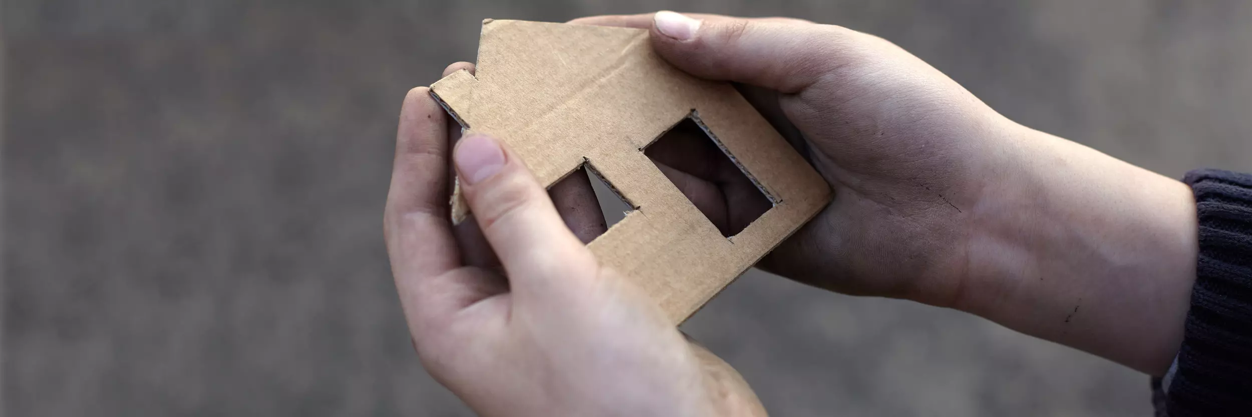 Eine Hand hält ein Haus aus Karton was symbolisch für ein Kinderheim steht.