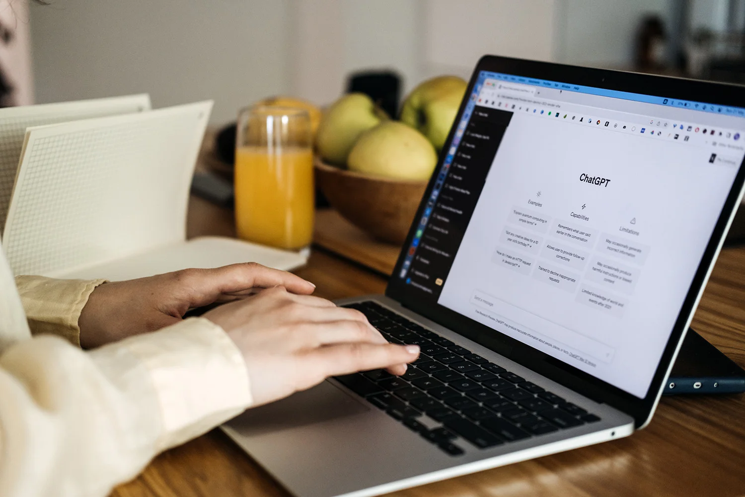 Ein Notebook auf eine Arbeitstisch. Zwei Hände bedienen die Tastatur, während der Display die Website von ChatGPT anzeigt.