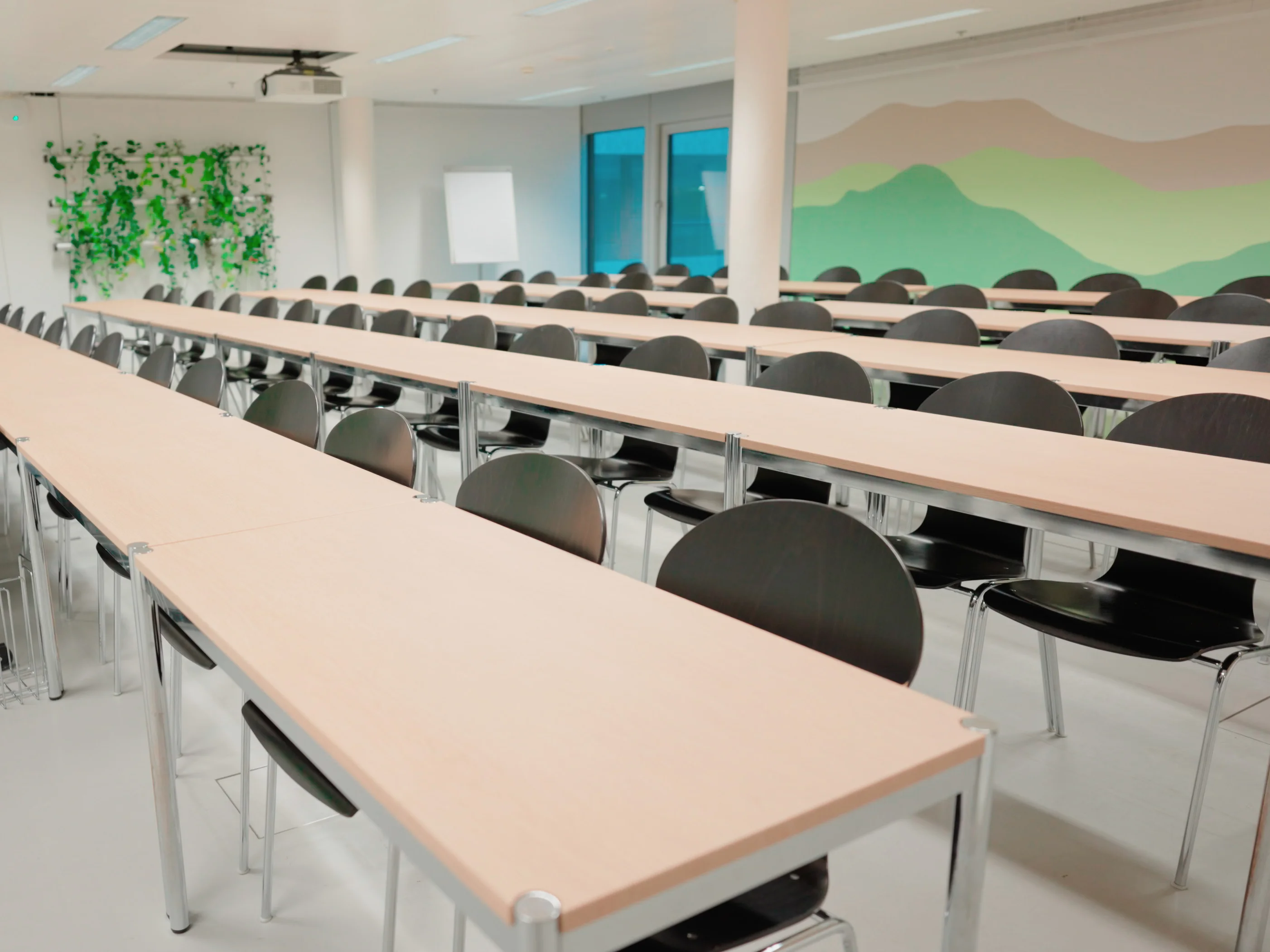 Bild eines Klassenzimmers mit biophilem Design: Holztisch, Wand mit gemalten grünen Bergen und Pflanzen.