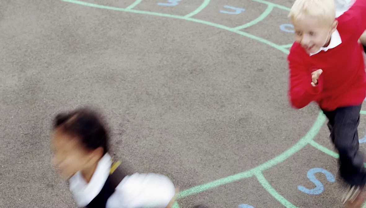 Kinder rennen einander hinterher auf einem Schulhof.
