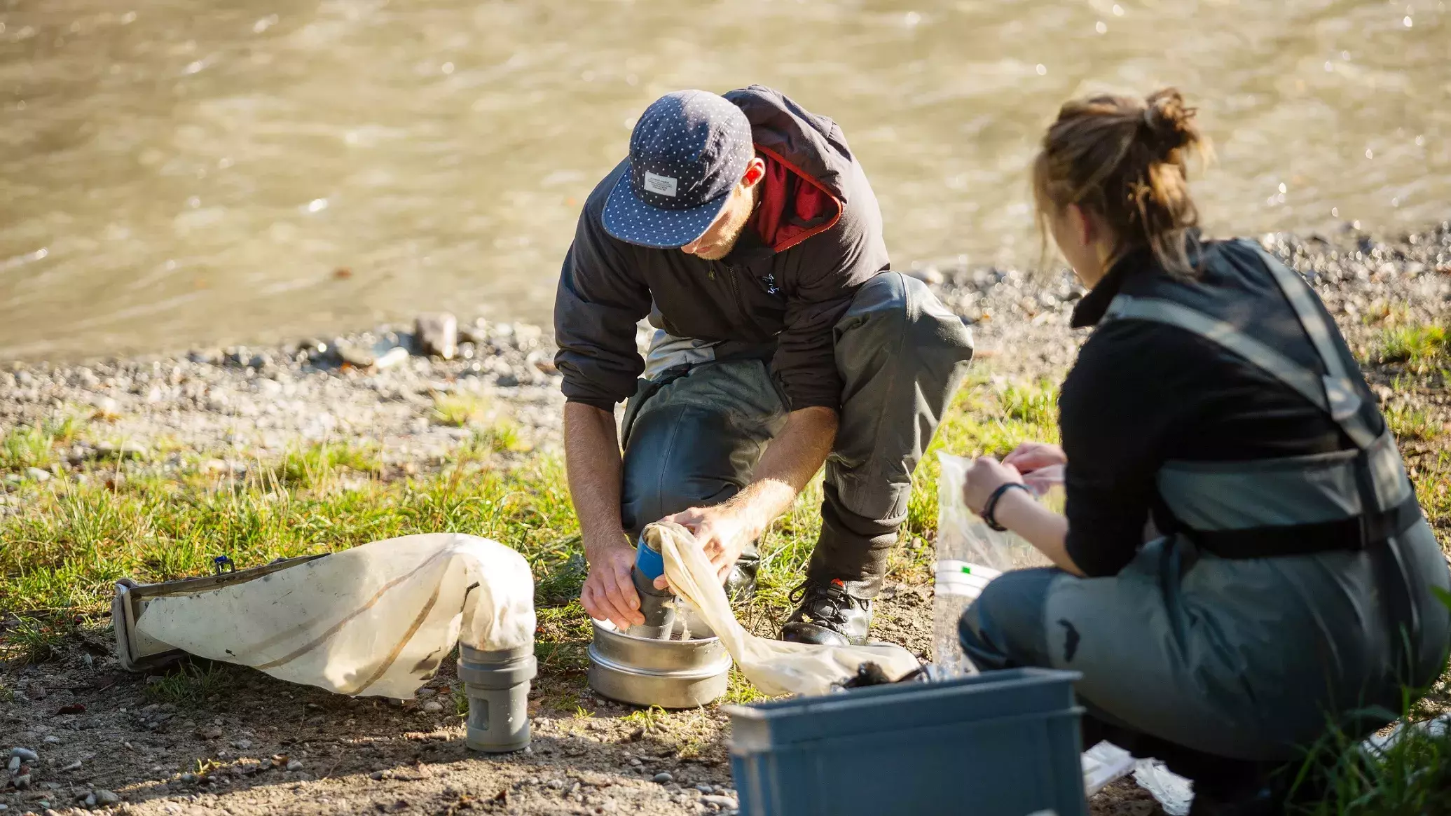 Zwei Personen sitzen neben einem Fluss und werten die Daten ihrer Messungen aus.