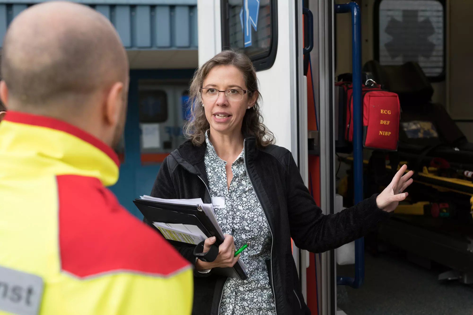 Kursleiterin Claudia Putscher erklärt den Sanitätern den Ablauf, sie stehen vor dem Rettungswagen.