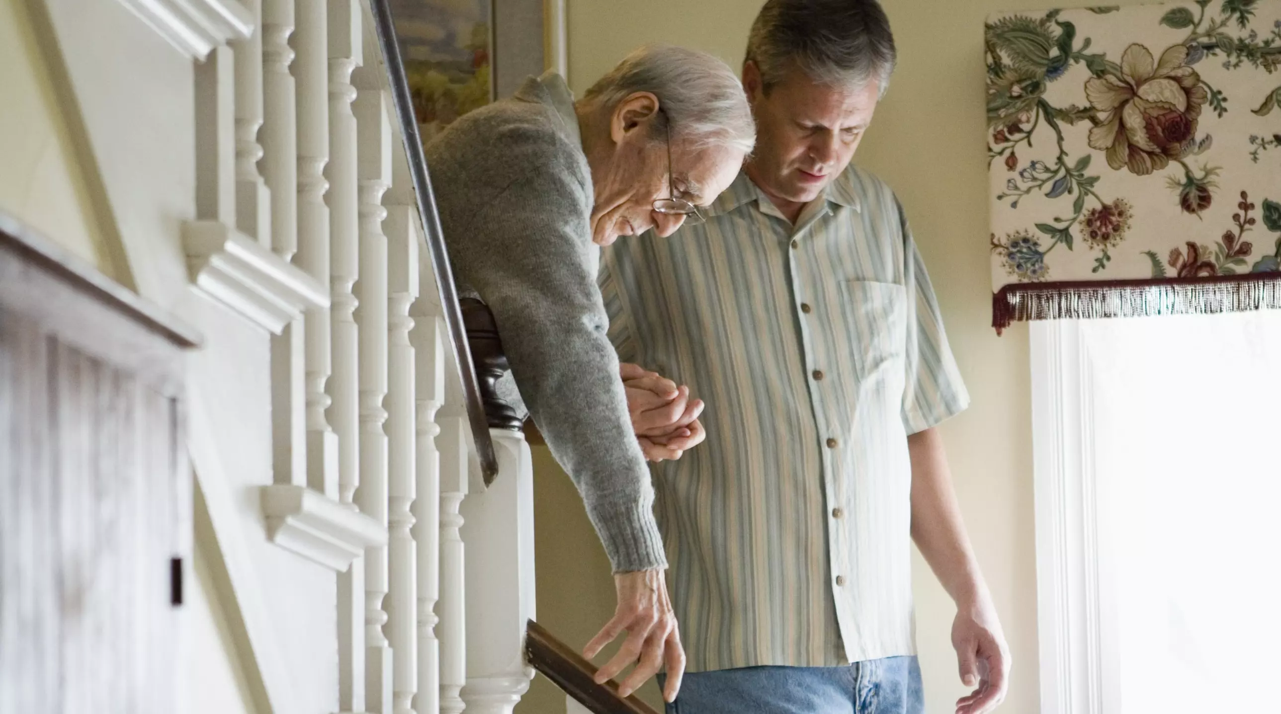 Mann hilft einem alten Mann die Treppe hinunter in einem Wohnhaus.