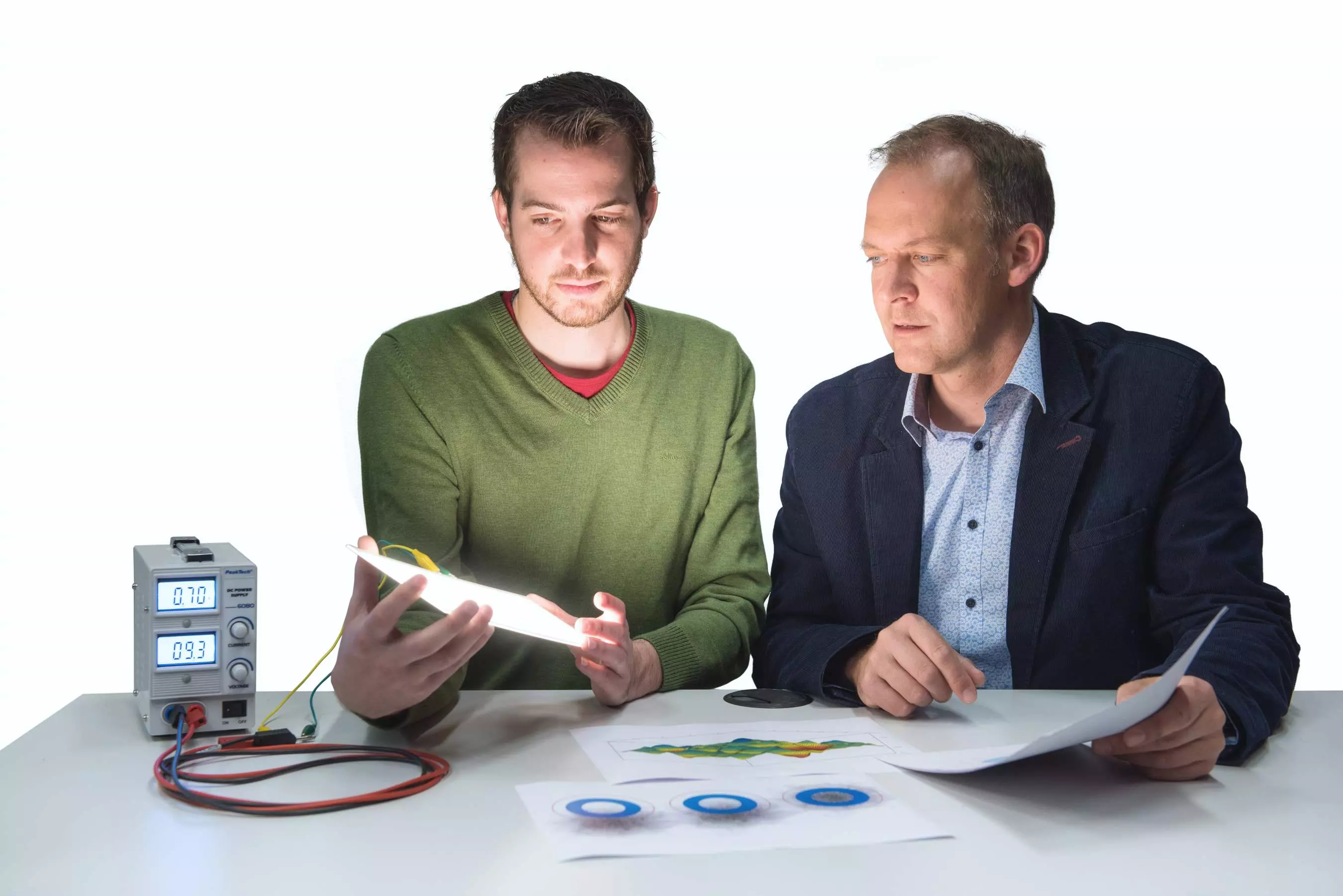 Student hält eine leuchtende OLED in der Hand und ein Dozent schaut ihm dabei über die Schulter