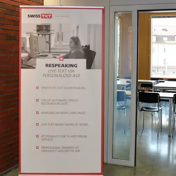 Vor der Türe zum Demoraum steht ein 2m hohes Plakat mit dem Titel: Swiss TXT. Respeaking. Live-Text via personalized ASR.