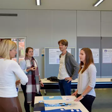 Konferenzbüro. Zwei Teilnehmende unterhalten sich mit zwei Personen des Konferenzteams.