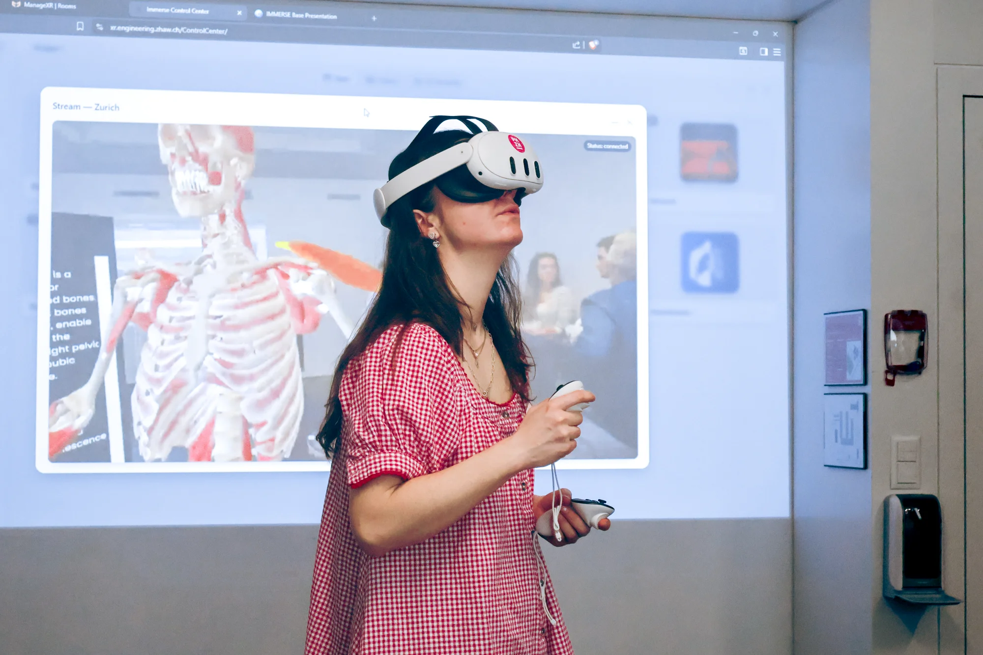 A person wearing a VR headset uses a virtual anatomy application in front of a projected image of a human skeleton.