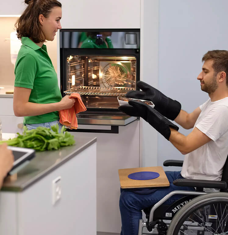 Person im Rollstuhl mit Therapeutin bei einer Übung in der Küche