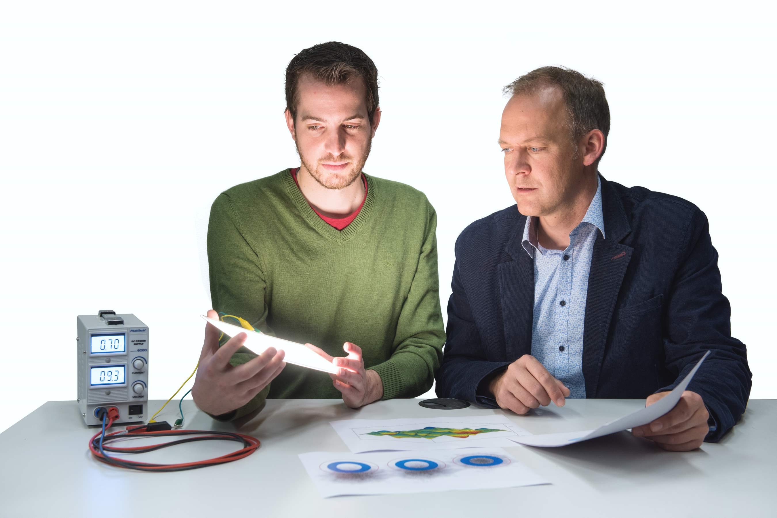 Student hält eine leuchtende OLED in der Hand und ein Dozent schaut ihm dabei über die Schulter