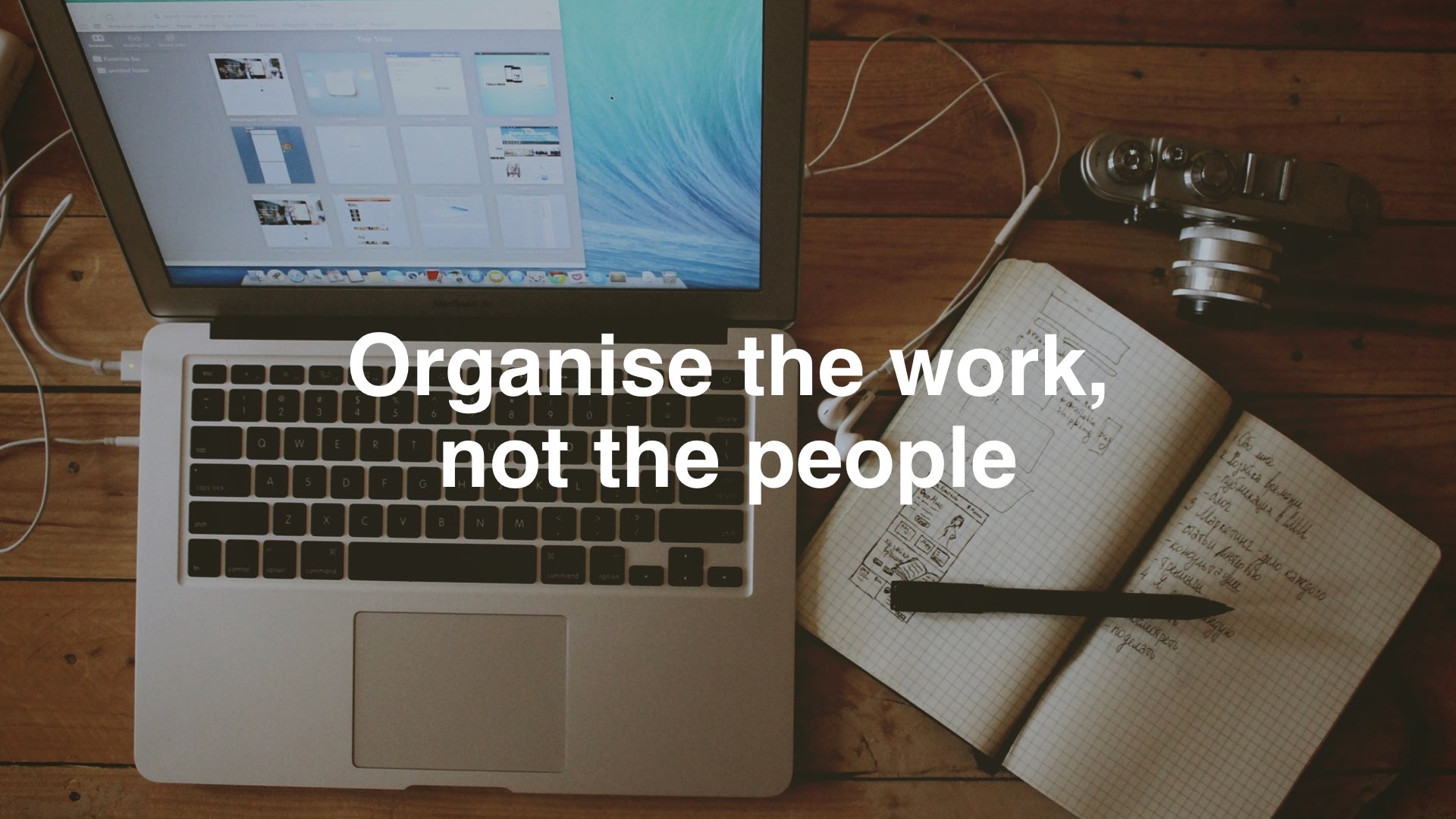 Ein Arbeitsplatz mit Laptop, Schreibgerät und Fotokamera. Auf das Bild geschrieben ist "organize the work, not the people".