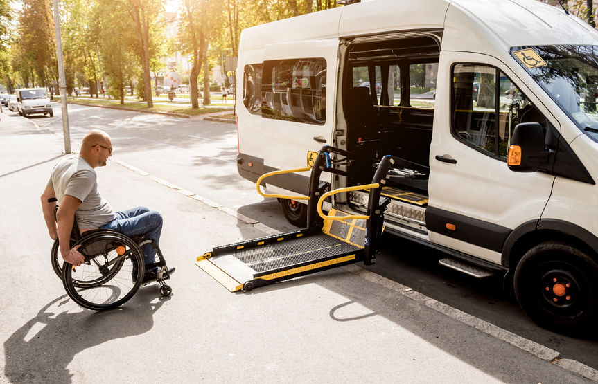 Bild mit Mann im Rollstuhl vor einem Fahrzeug des eines Behindertenfahrdiensts
