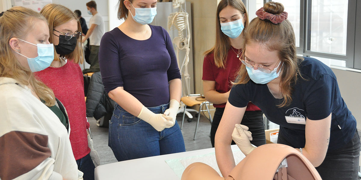 Eine Hebammenstudierende zeigt an einem Modell, wie eine vaginale Untersuchung abläuft.