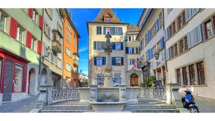 Blick auf einen Brunnen in der Altstadt von Zürich mit farbigen historischen Häusern im Hintergrund