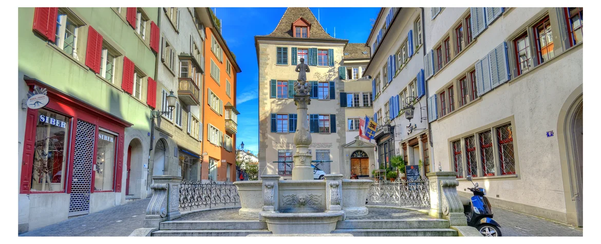 Blick auf einen Brunnen in der Altstadt von Zürich mit farbigen historischen Häusern im Hintergrund