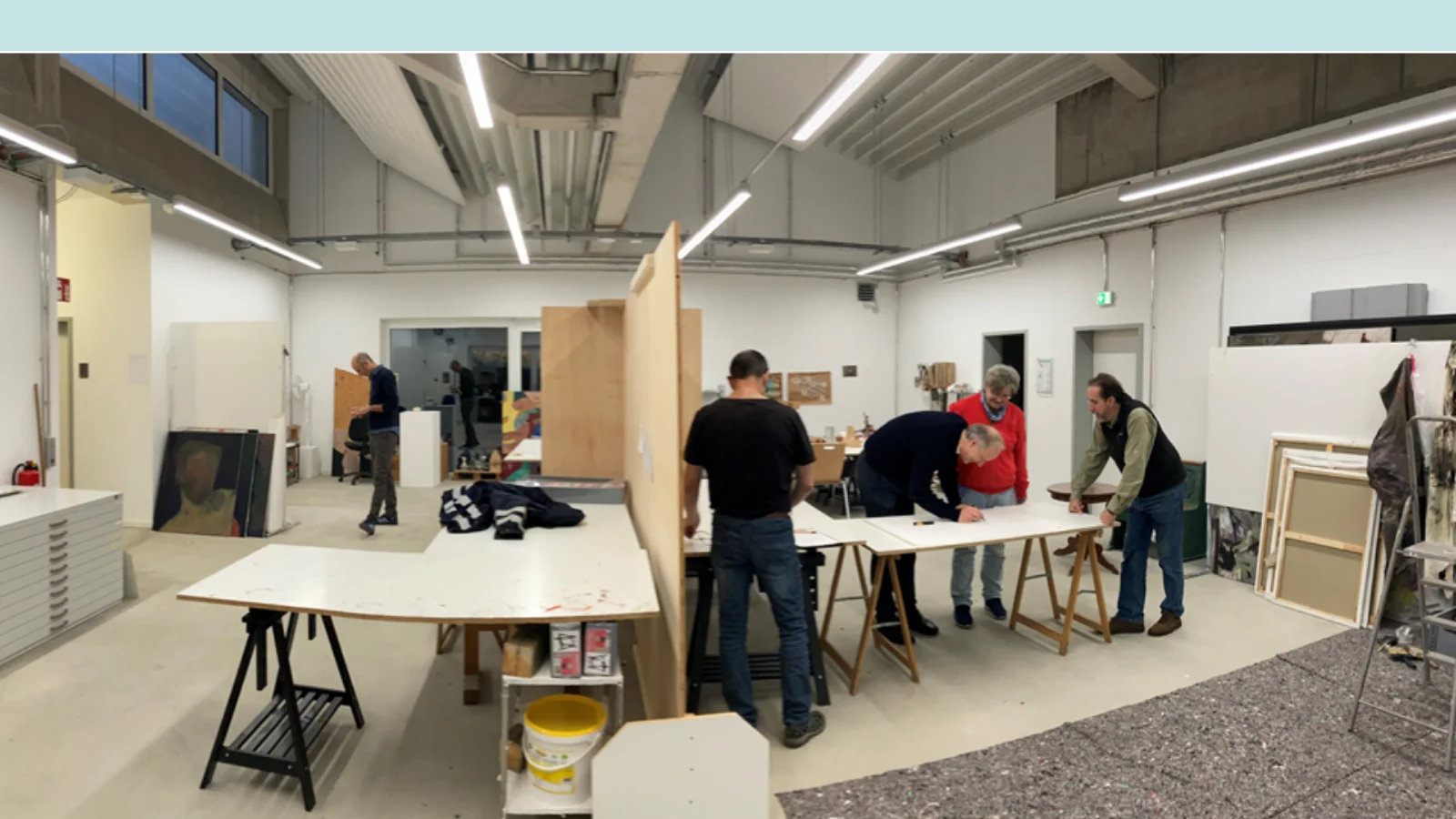 Ein Raum mit Tischen und Trennwand. Teilnemende des Workshops arbeiten stehend an einem Tisch.