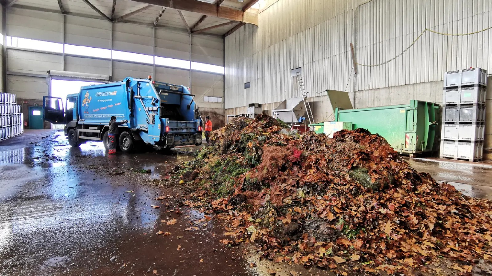 Hall with a pile of green waste on wet floor and a blue truck