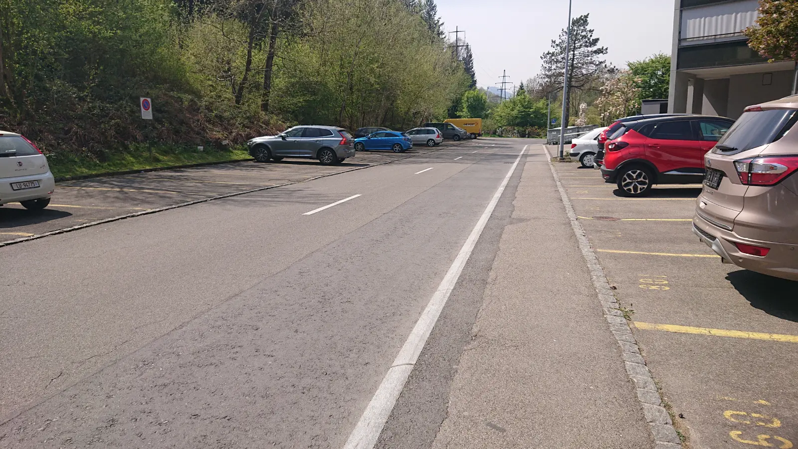 A road and to the left and right of it car parks with parked cars.