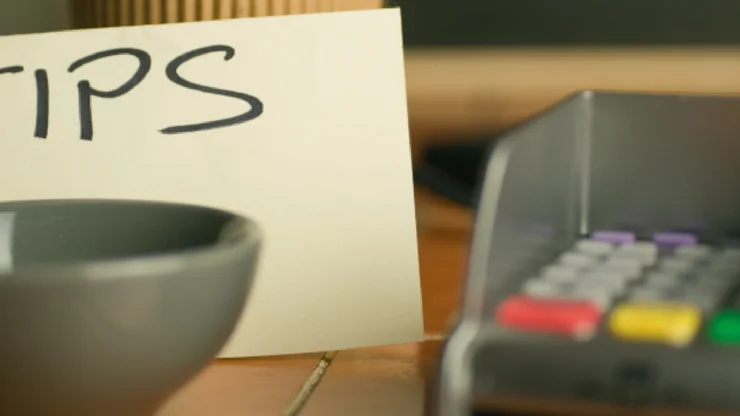 Auf einem Zettel steht "Tips" und davor eine leere Trinkgeldschale und ein Zahlgerät für Karten.