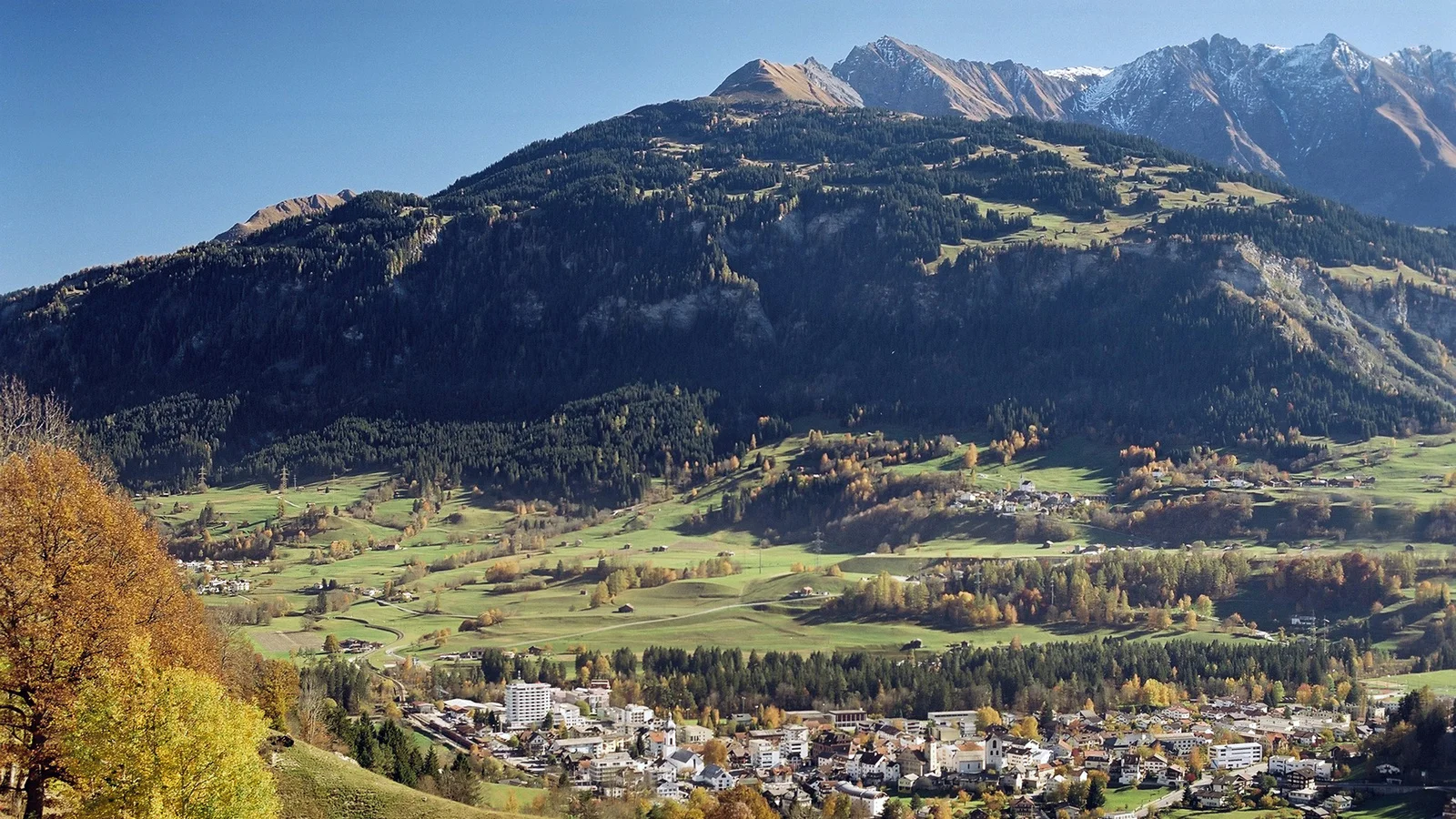 Im unteren Teil ist das Dorf Surselva zu sehen, dahinter erheben sich hohe Berge. 