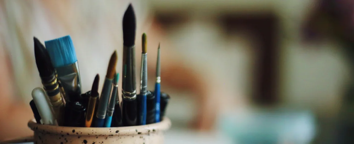 Ein Tonglas mit Pinseln drin vor einem unschaften Hintergrund.