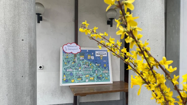 Das Bild zeigt im Vordergrund ein Forsythienzweig zwischen Betonpfeilern, im Hintergrund die Illustration der möglichen Ernährungsstrategien für Wädenswil