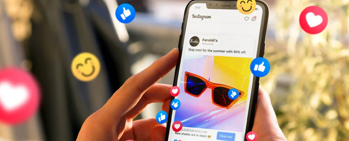A person holds a phone with both hands; On the phone you can see an advertisement for glasses; there are many emojis visible like thumbs-up, hearts and smilies