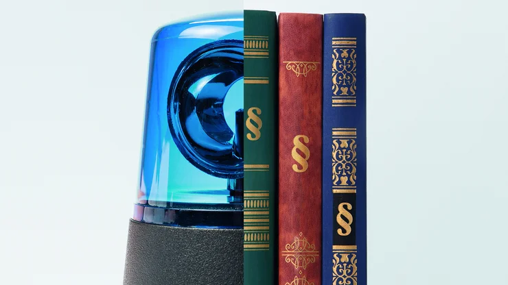 Eine blaue Polizei-Sirene steht neben drei juristischen Büchern.